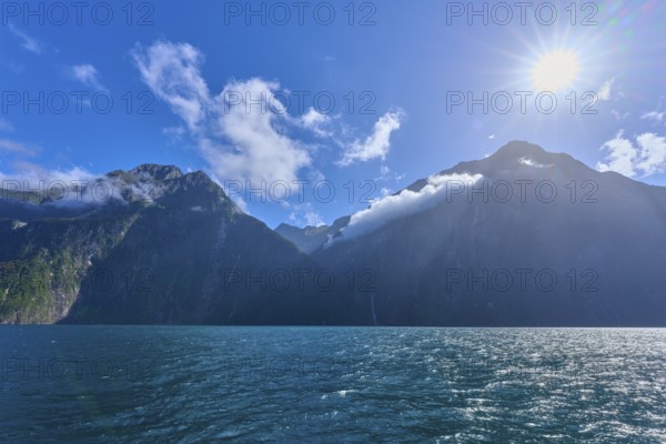 Bright sun over majestic mountains and calm sea, summer, Milford Sound, Te Anau, Fiordland National