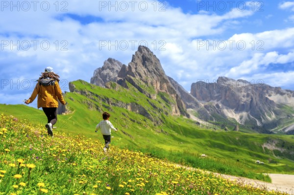 Tourists running through a field of wildflowers with the seceda peaks in the dolomites mountain