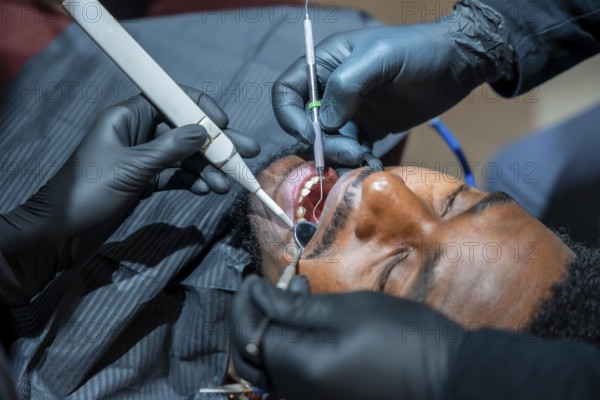 Close up of a dentist using specialized tools during a teeth whitening session on a male patient,