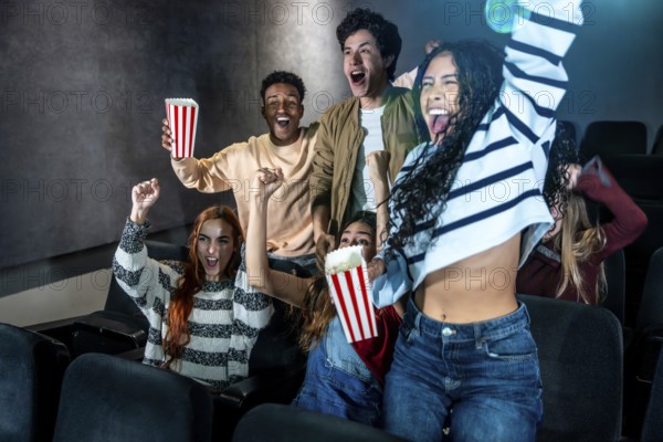 Excited friends cheering together during a movie night at the cinema, enjoying popcorn and sharing