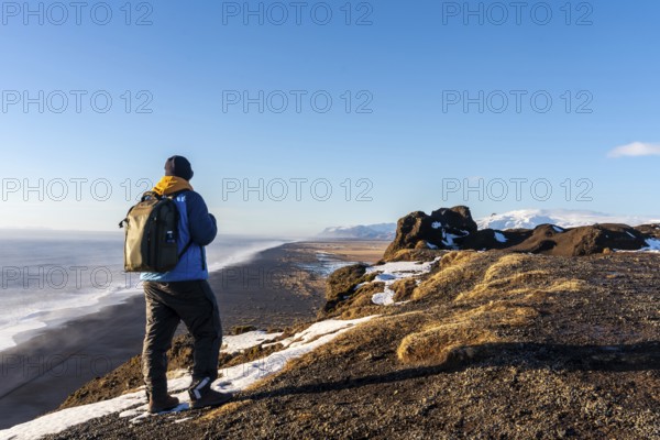 A tourist man with his back turned at the viewpoint of Dyrholaey beach in the cold winter with snow