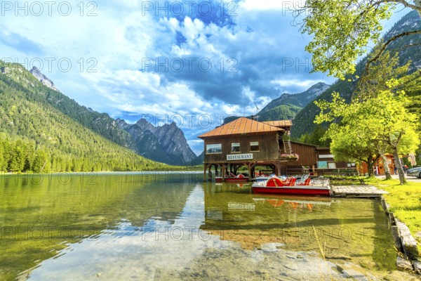 Stunning view of lake dobbiaco with pedal boats and a restaurant, surrounded by the majestic peaks