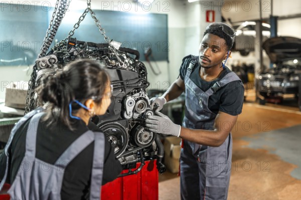 Two focused mechanics examining a car engine hanging from a crane in a professional workshop,