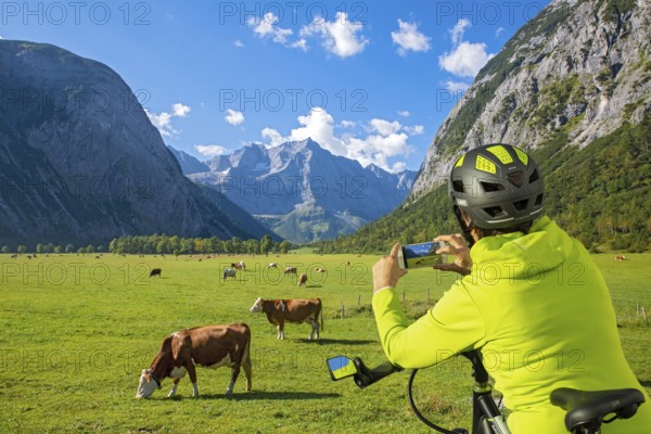 A biker uses her mobile phone to photograph the Großer Ahornboden and the grazing cows, Großer