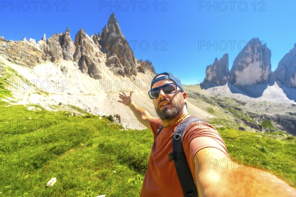Hiker taking a selfie with the tre cime di lavaredo in the background, during a summer hike in the