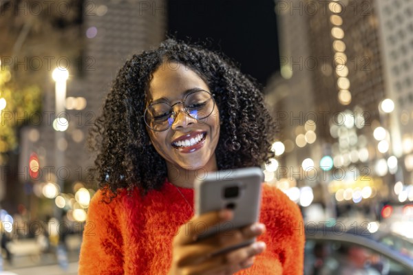 Smiling woman using her smartphone while enjoying the vibrant urban nightlife, surrounded by
