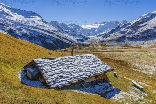 Alpine hut with snow-covered roof, slightly snow-covered alpine meadow, behind the Moiry glacier,