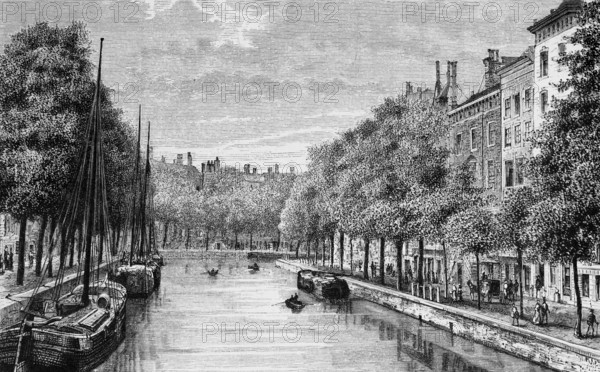 Tree-lined canal in the Dutch capital Amsterdam, cargo ships, promenade with pedestrians,