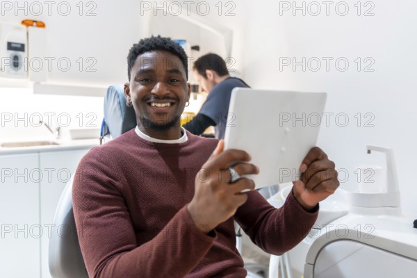 Smiling patient using digital tablet, possibly reviewing treatment plan or x rays, while dentist