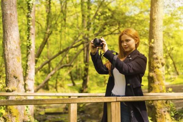 Woman photographer with a black jacket enjoying in an autumn park, taking pictures at sunset on a