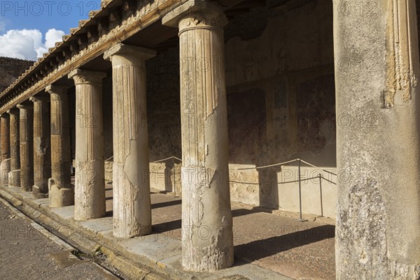 Old large building covered with terracotta clay roof tiles and supported by stone columns at the