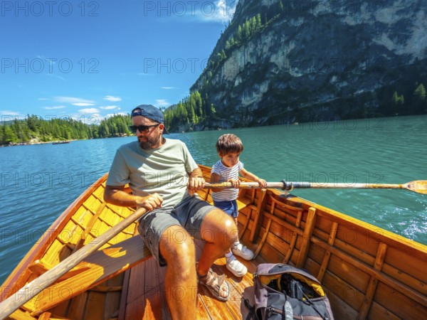 Father and son enjoying a summer day rowing a wooden boat on lake braies with the stunning
