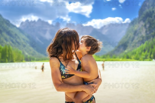 Mother embracing and kissing her son while enjoying summer vacation at lago di landro, surrounded