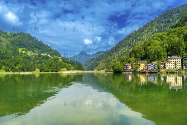 Tranquil summer scene at lake alleghe with colorful houses reflected in the emerald water,