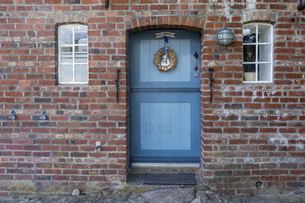 Blue wooden door in red brick wall with two windows and decorations, Föhr, Nordfriesland,