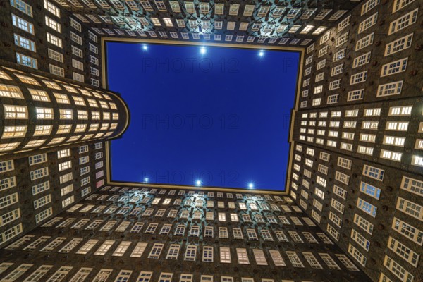 Symmetrical inner courtyard of a Kontorhaus with illuminated rows of windows at night, Hamburg,