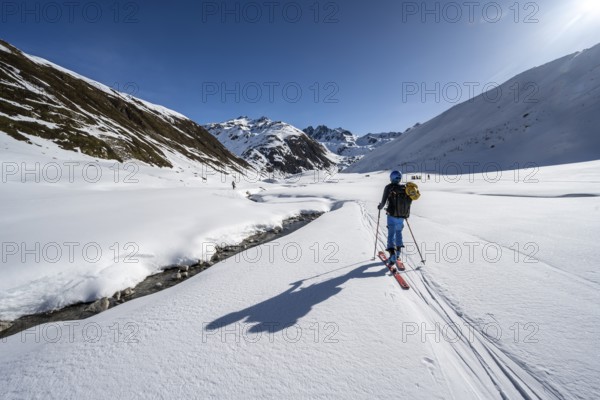 Ski tourer in the snow by a mountain stream in the Funtauna Valley, Graubünden Haute Route, Albula