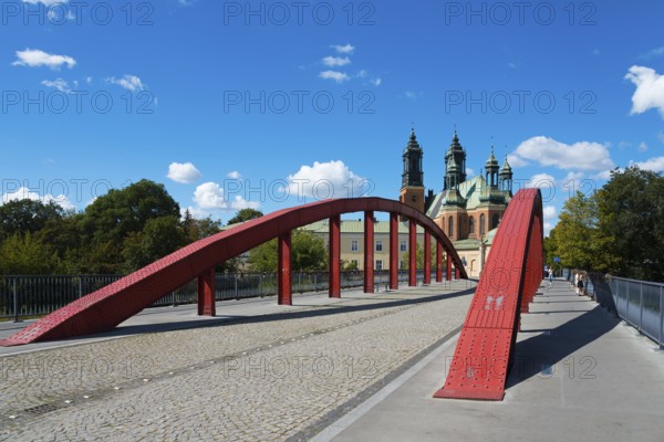 A modern red bridge leads to the cathedral in the background with blue sky and white clouds,