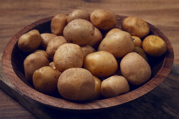 A wooden bowl filled with freshly harvested small potatoes sits on a rustic wooden surface,