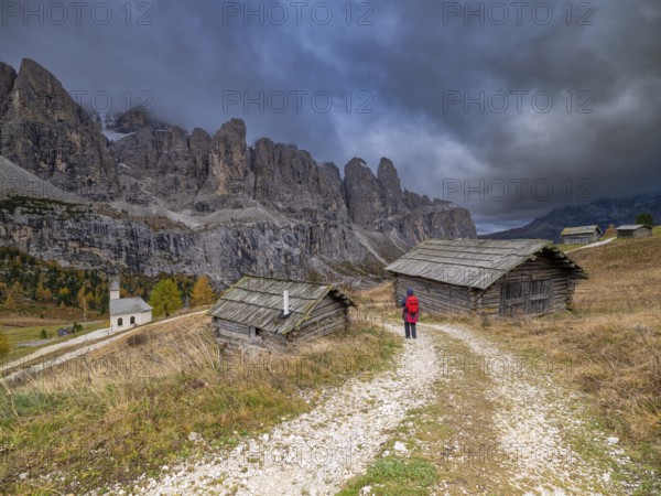 Hiker in front of two huts at the Gardena Pass, chapel, gloomy clouds, Passo Gardena, autumn, Sella