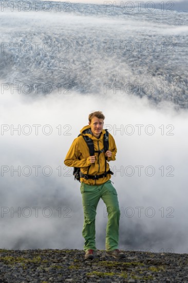 Young man in front of impressive landscape at sunset, fog, clouds moving around, glacier ice of the