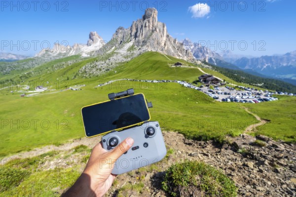 Hand piloting a drone with a smartphone attached to the controller in the scenic landscape of giau