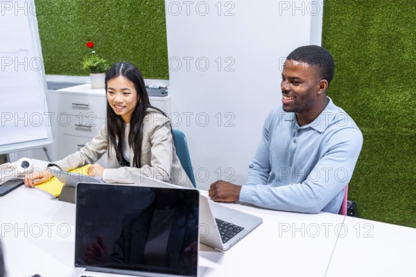 Two businesspeople are working together on a project in a modern coworking office, using laptops