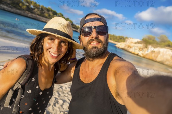 A man and woman are posing for a picture on a beach. The man is wearing a black tank top and