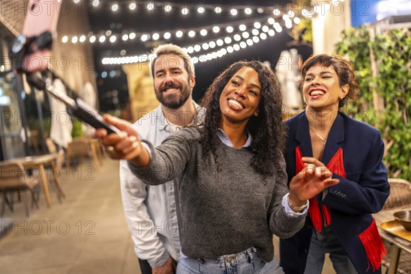 Latin woman streaming online during night party with multi-ethnic friends in the roof terrace of a