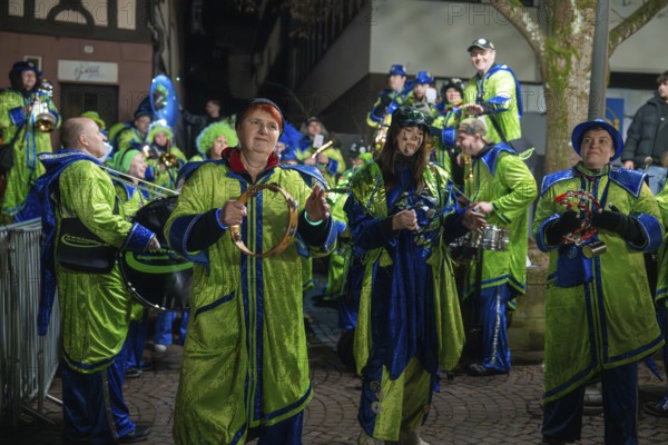 Music group in green and blue costumes with instruments at a night-time performance, carnival,
