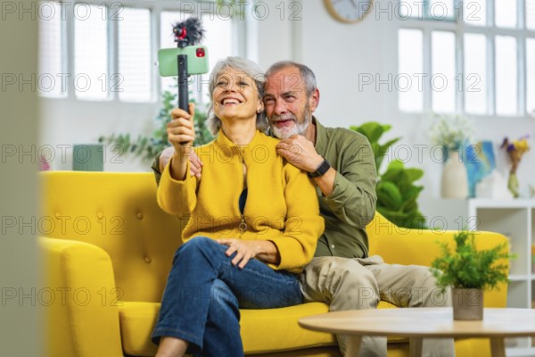 Happy senior couple during online meeting with the family using smartphone sitting on the sofa