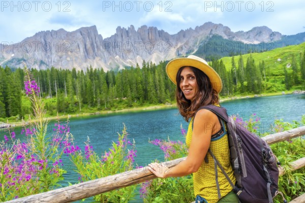 Female tourist with backpack and straw hat enjoying the landscape of lake carezza and latemar