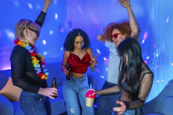 Cheerful multi ethnic friends dancing together and enjoying drinks at a home disco party with blue
