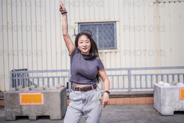 Asian young woman pointing to the sky dancing k-pop urban dance outside an industrial building in