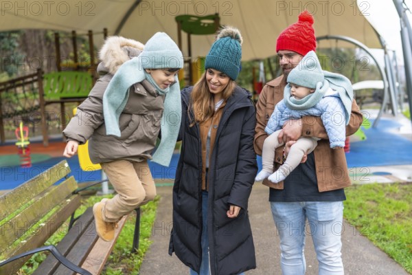 Smiling family enjoying a joyful winter day at the playground, with children happily jumping on a