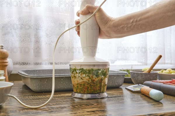 A hand blending device is being used to process fresh herbs and vegetables in a well-organized