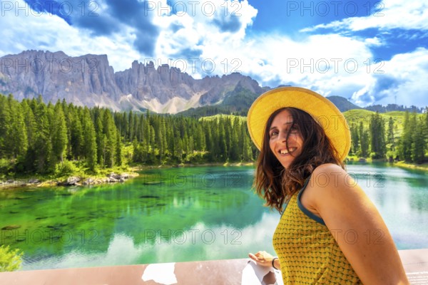 Tourist admiring the stunning emerald waters of lake carezza, with the latemar mountain range in