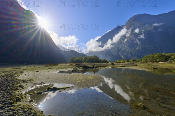 Dramatic sunbeams over mountains with clouds and water reflection, summer, Milford Sound, Te Anau,