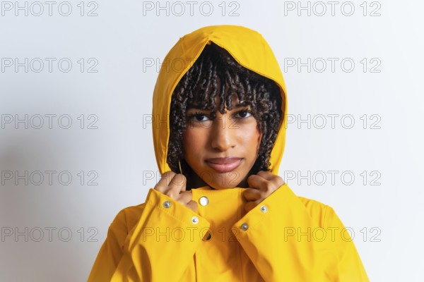 Studio portrait of a young woman with curly hair wearing a yellow raincoat and pulling the hood