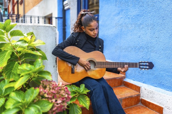 African american young beauty woman playing acoustic guitar outside a colorful house