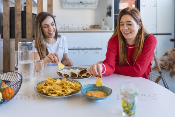 Two cheerful women enjoying a meal of quesadillas, nachos and sauce, creating a cozy and joyful