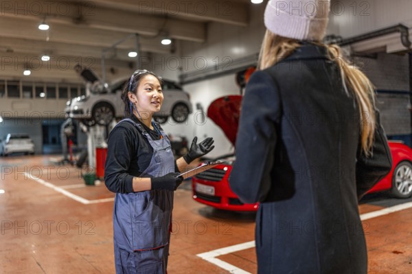 Professional female mechanic explaining car repair details to customer, holding clipboard in auto