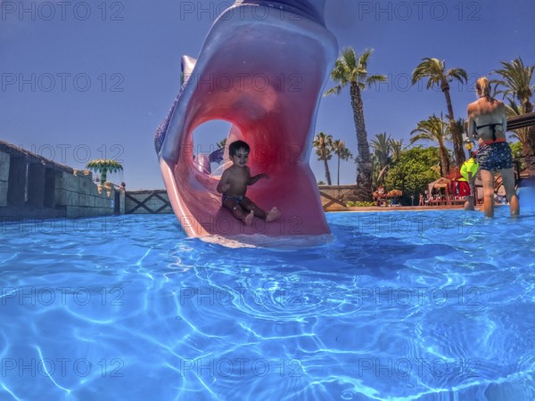 Young boy enjoying summer vacation sliding down a waterslide shaped like a monster's mouth into a