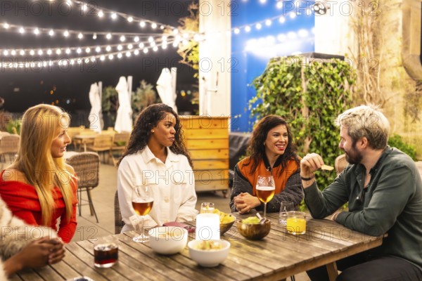 Multi-ethnic male and females friends talking relaxed drinking alcohol and eating snacks in a night