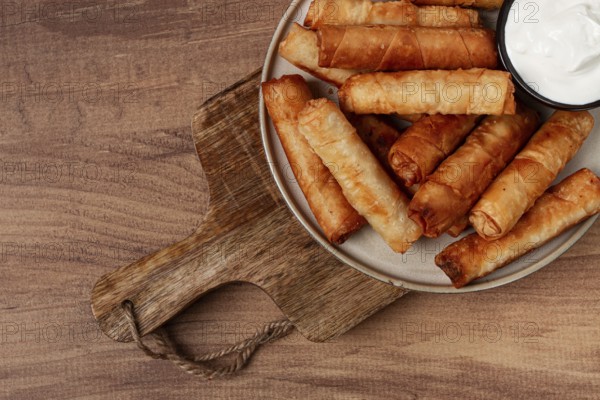 Fried spring rolls with cheese, on a wooden background, with cream sauce, no people