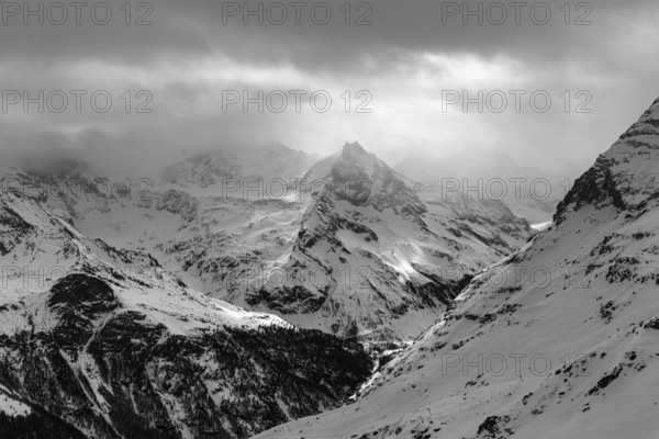 Dark clouds and wafts of mist surround the snow-covered summit of Mount Le Besso, view from the