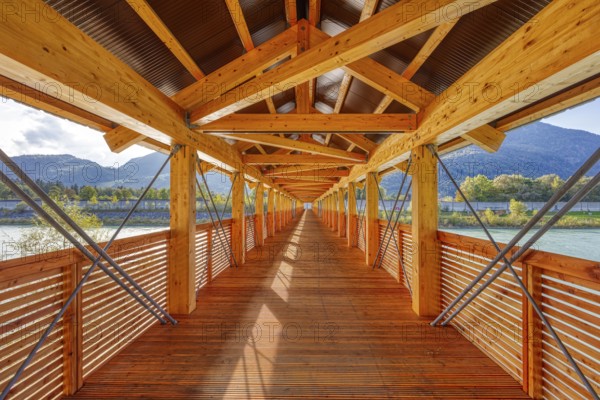 Perspective of a wooden bridge, framed by mountains and river, with modern construction, Inn