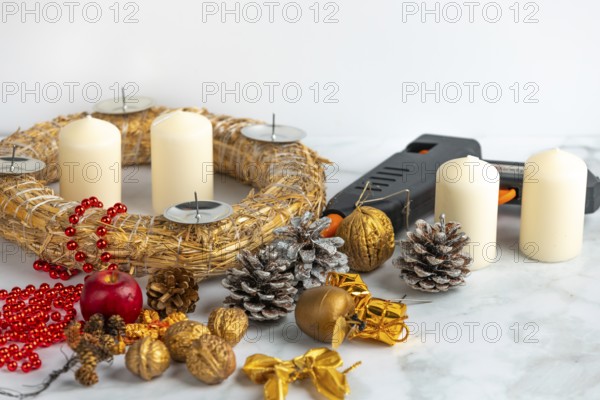 Craft scene with Advent wreath, white candles, decoration material and a glue gun on a marble