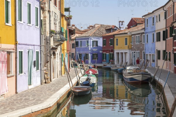 Colourful houses along a quiet canal with parked boats on the island of Burano, Venice, Italy,