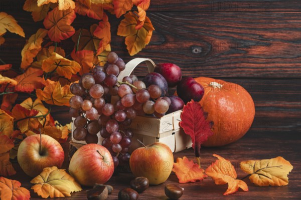 A basket of grapes and plums next to a pumpkin, apples, chestnuts and autumn leaves